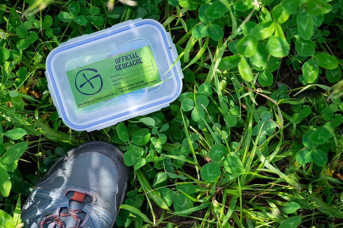 Transparent geocache container with a green sticker in clover, with a hiking shoe beside it